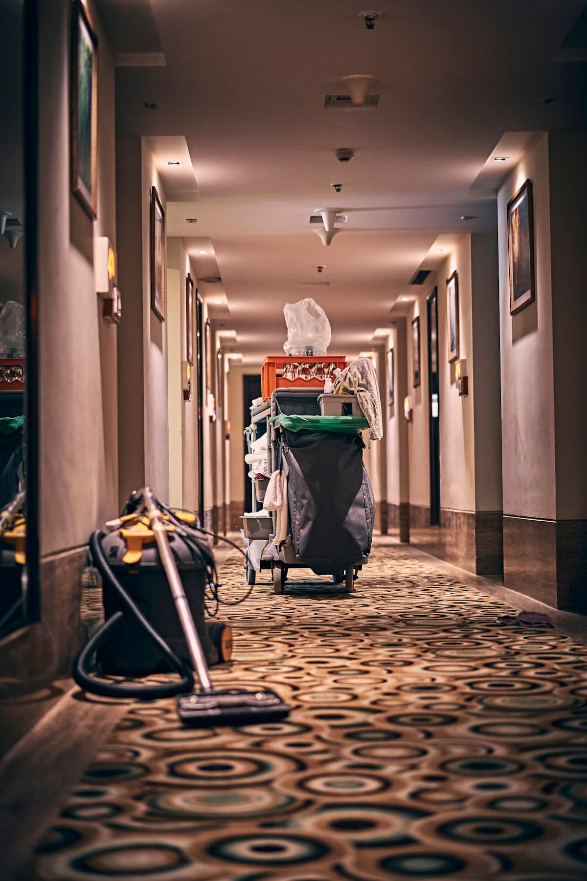 A housekeeping cart and vacuum in a long carpeted corridor