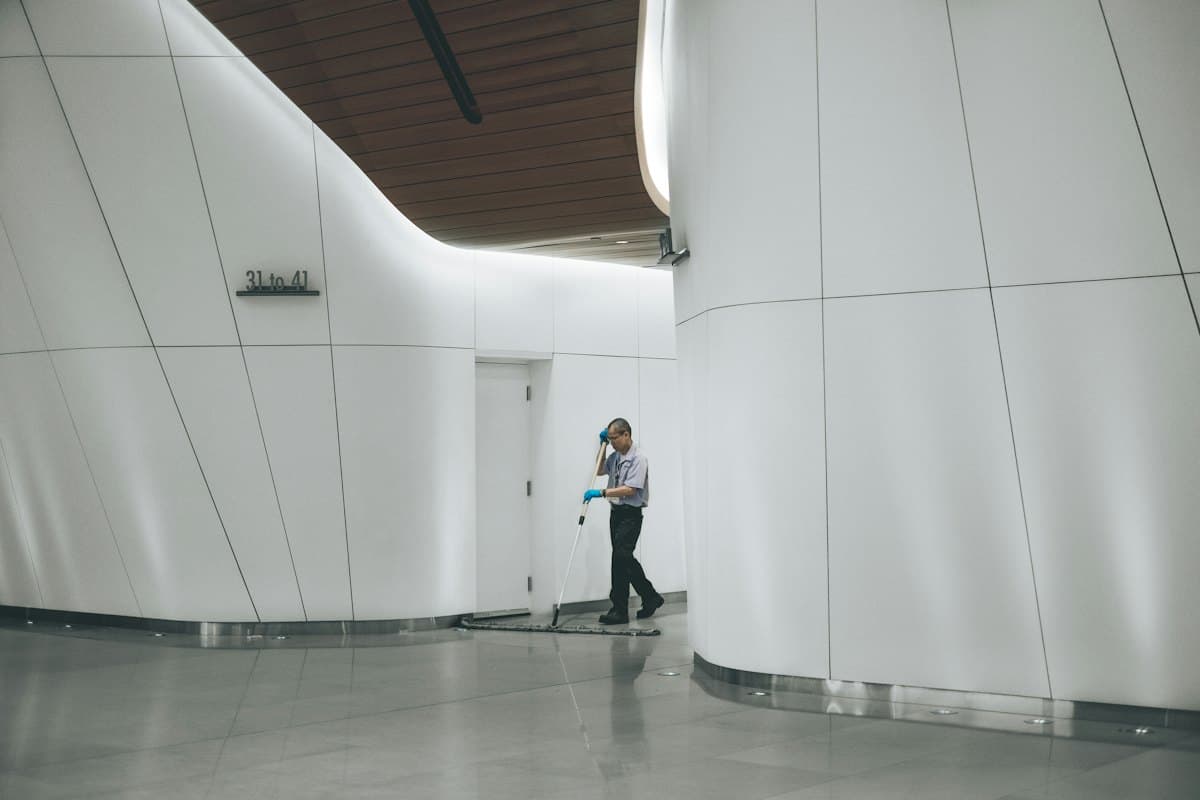 A worker cleaning a floor beside a bare white wall during a building fit-out