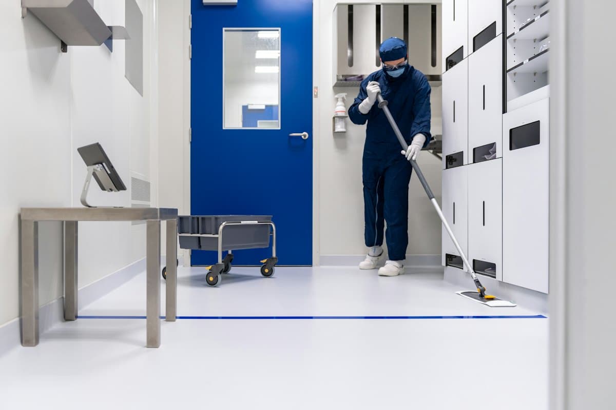 A worker in protective coveralls mopping a sterile white floor